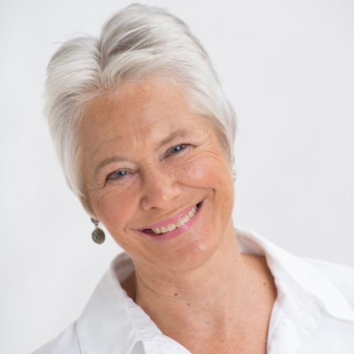 Gail Straub is a woman with light skin tones, short white hair and blue eyes. She's wearing earrings and a white blouse